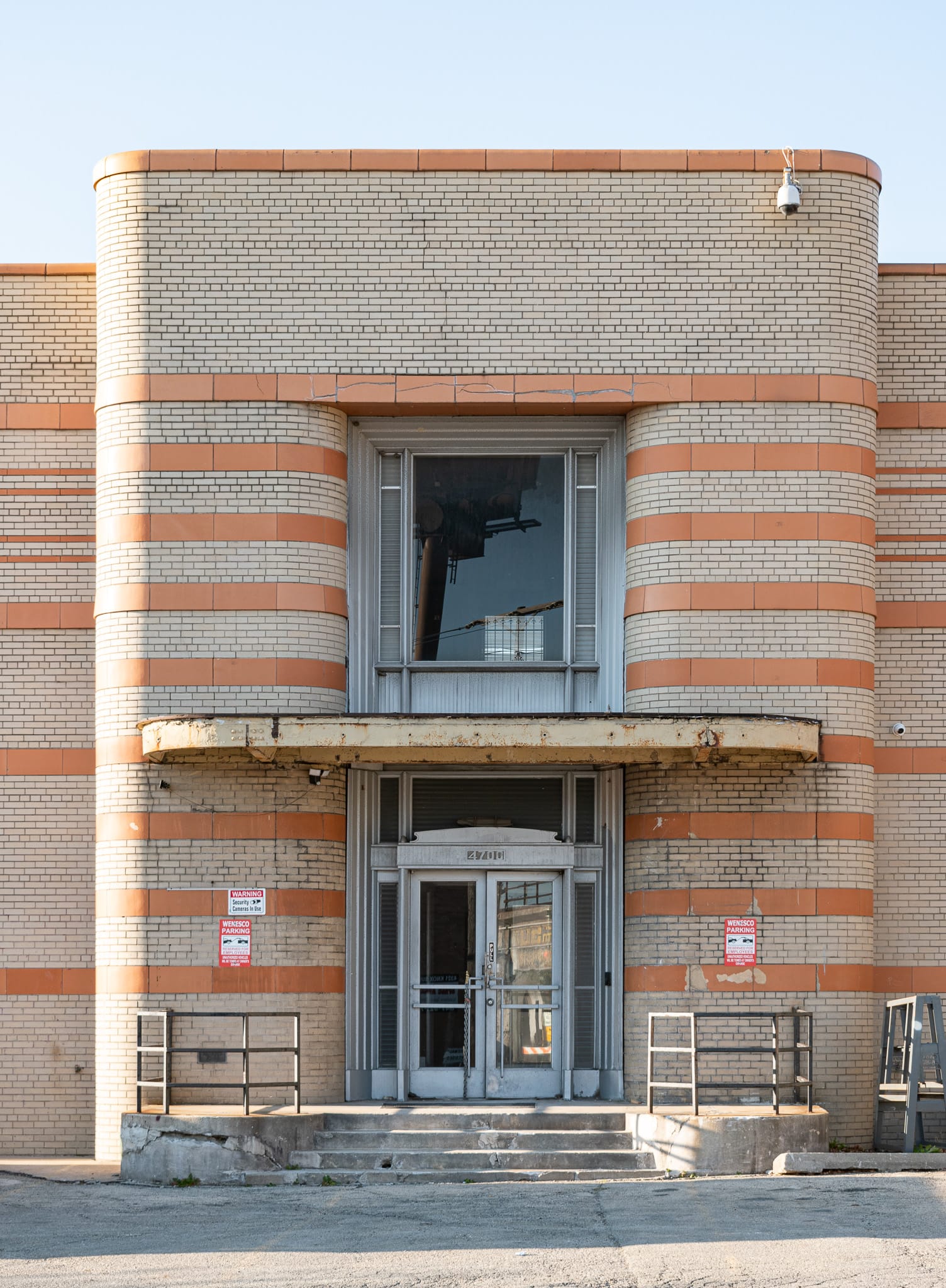 2020 photo of the front entrance with slightly crumbling concrete stairs and a rusting metal canopy. 