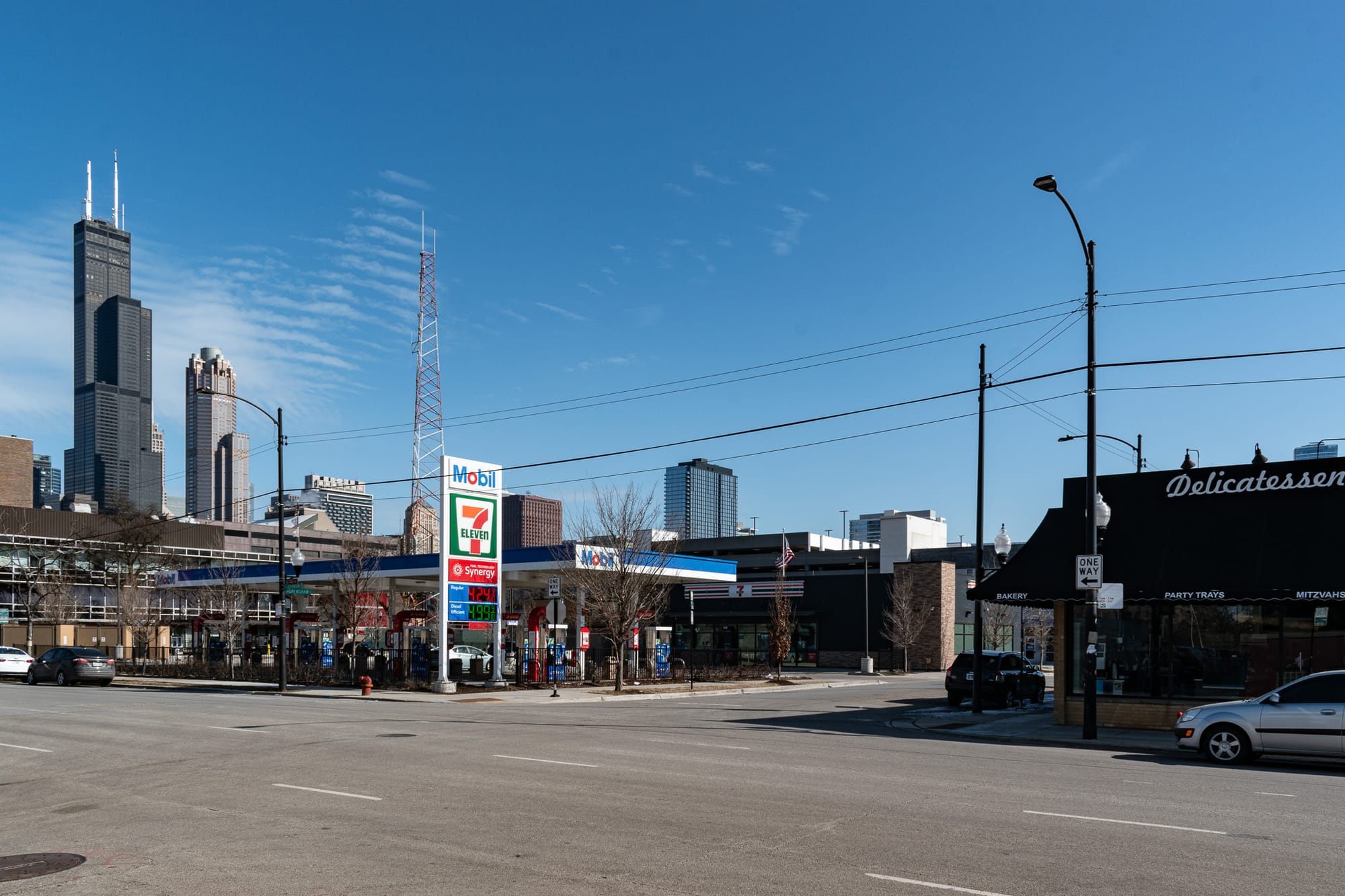 South Loop street scene looking west on Grenshaw from Jefferson, with Manny's Deli on the right and a Mobil filling station in the center. The Willis Tower and 311 S. Wacker prominent in the background. 